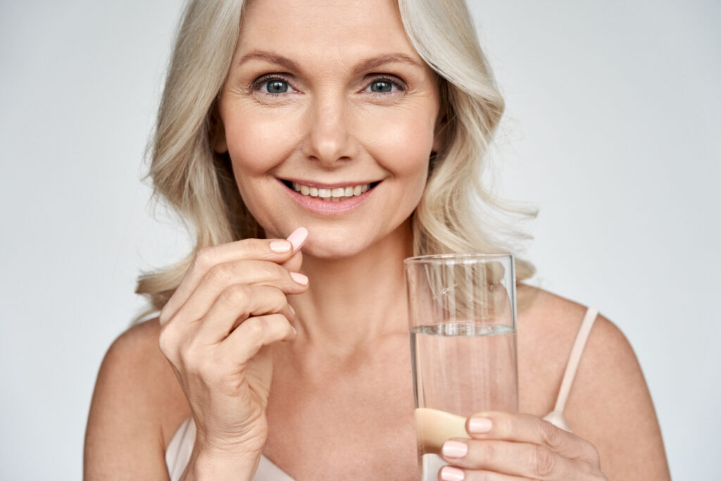 Middle aged woman hydrates and takes a vitamin during her facelift recovery. Middle aged woman hydrates and takes a vitamin during her facelift recovery.